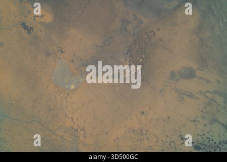 Vista aerea di un paesaggio asciutto con consistenza del terreno crepata e macchie di fango secco. La superficie mostra modelli di erosione e fratturazione naturale tipica delle aree aride o colpite dalla siccità Foto Stock