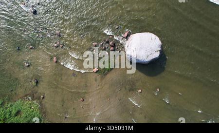 Vista aerea dell'enorme masso costiero circondato da acque basse e onde in Estonia Foto Stock