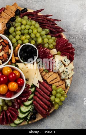 Un colorato tagliere di salumi è distribuito con vari tipi di carni, formaggi, uva fresca, olive e pomodori ciliegini, perfetto per la condivisione in un ambiente informale Foto Stock