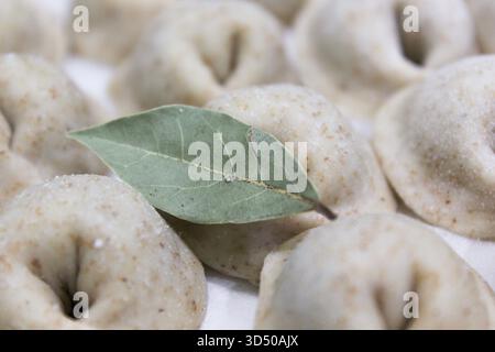 I gnocchi poggiano su una superficie, mostrando le loro forme uniche come una singola foglia di alloro aggiunge un tocco aromatico. L'atmosfera accogliente della cucina invita a un senso di benessere Foto Stock