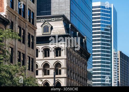 Montreal, Canada - 11 agosto 2025: Storico edificio in pietra con finestre ad arco circondato da moderni grattacieli in vetro nel centro di Montreal Foto Stock