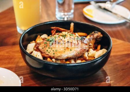 Tradizionale poutine del Quebec con confit di anatra servita in una ciotola nera in un ristorante Foto Stock