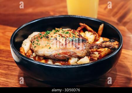 Tradizionale poutine del Quebec con confit di anatra servita in una ciotola nera in un ristorante Foto Stock