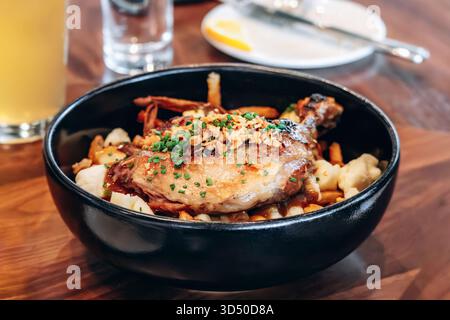 Tradizionale poutine del Quebec con confit di anatra servita in una ciotola nera in un ristorante Foto Stock