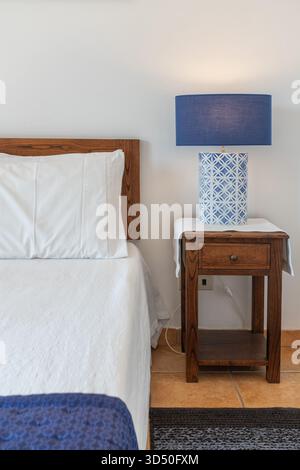 I soffici letti bianchi accentuano l'atmosfera invitante di questa accogliente camera da letto con comodino in legno e un'elegante lampada blu sul lato Foto Stock
