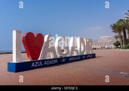 Il cartello i Love Agadir, con la kasbah Agadir Oufella sulla collina in lontananza, sul lungomare Foto Stock