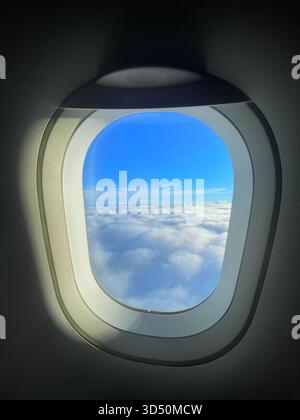 Vista dalla finestra dell'aeroplano che mostra il cielo azzurro e gli strati di nuvole, catturando la serenità del viaggio in alta quota Foto Stock