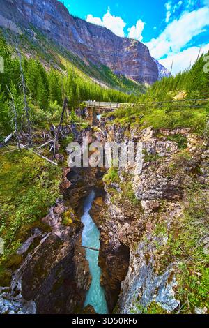 River Canyon con Bridge Lush Forest e torreggiante paesaggio montano Foto Stock