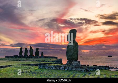 Statue moai presso il sito archeologico AHU Tahai sull'Isola di Pasqua (Rapa Nui), Cile. Un moai solitario si erge in primo piano contro un tramonto spettacolare e colorato Foto Stock