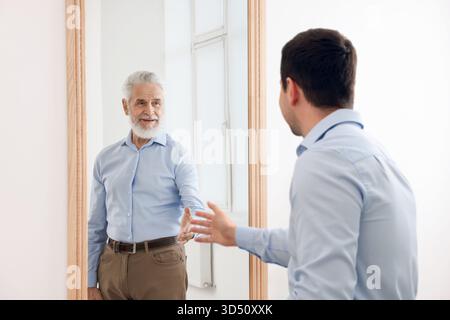 Il giovane si vede come un anziano allo specchio. Concetto di personalità, passato e futuro, flusso del tempo, età Foto Stock