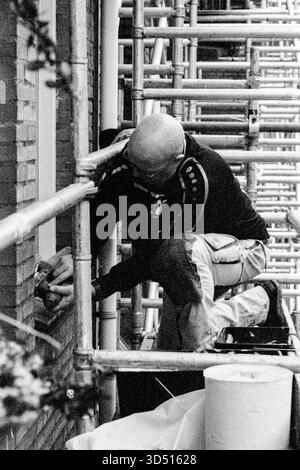 Pittore che lavora su ponteggi. Pittore industriale e operaio edile, che lavora su un lavoro immobiliare domestico da una struttura a tre piani di ponteggi. Tilburg, Paesi Bassi. Girato su Analog Black & White Film, 2022. Tilburg Studio Tuinstraat Noord-Brabant Nederland Copyright: XGuidoxKoppesxPhotox Foto Stock