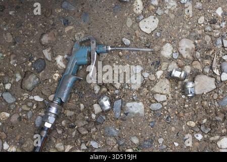 Pistola ad aria compressa sporca, utensile pneumatico per lavori industriali, appoggiata a terra. Questa attrezzatura usata in officina poggia su un attrezzo sporco, grintoso e dimenticato Foto Stock