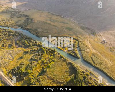 Una vista aerea di un fiume turchese che si snoda attraverso le isole di lussureggiante vegetazione e pennello giallo in un'ampia e asciutta fondovalle, in contrasto con barre Foto Stock