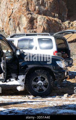 Naryn, Kirghizistan - 12 novembre 2025: La vista laterale di una Toyota Land Cruiser 100 nera parcheggiata accanto a un SUV bianco, con il bagagliaio del SUV bianco op Foto Stock