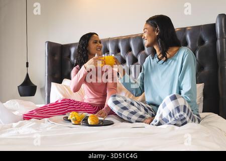 Bicchieri con diversi amici femminili seduti in camera da letto, con vassoio per la colazione con succo di frutta e frutta Foto Stock