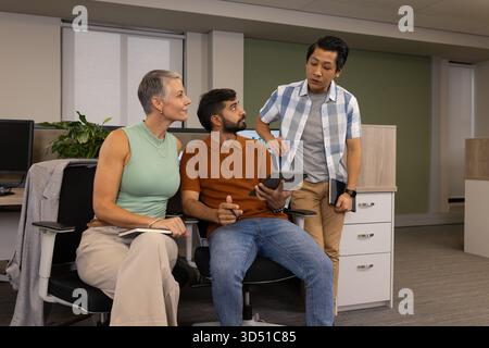 Diversi colleghi che collaborano intorno a una workstation in ufficio, con tablet e notebook Foto Stock