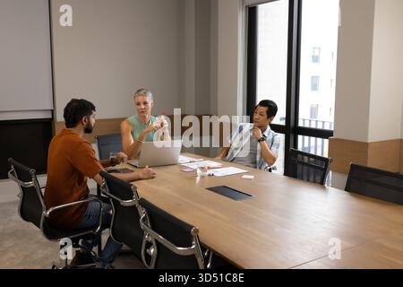 Discutere di diversi colleghi che si riuniscono attorno a un tavolo in legno in ufficio, con un laptop e un pennarello rosso Foto Stock