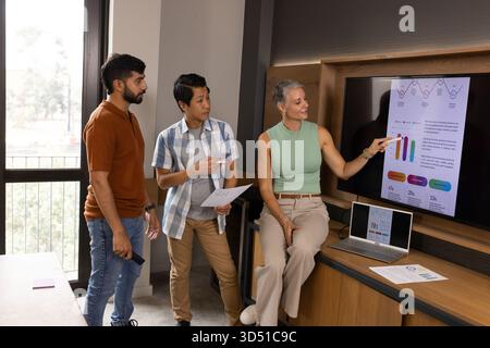 Presentazione di colleghi diversi che puntano sulle carte nella moderna sala conferenze, con computer portatile e report Foto Stock