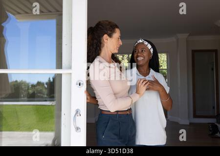 L'agente immobiliare e il cliente sorridono nell'ingresso della casa, con porta in vetro incorniciato e fascia a motivi geometrici Foto Stock