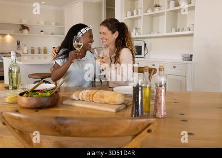 Alzare bicchieri da vino diverse amiche sedute al tavolo della cucina, con pane affettato Foto Stock