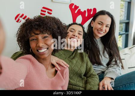 Diverse donne e amici che indossano fasce elastiche che scattano selfie sul divano di casa tenendo in mano lo smartphone Foto Stock