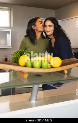 Baciare diverse donne nell'isola cucina grigia, con ciotola di frutta in legno e smartphone Foto Stock