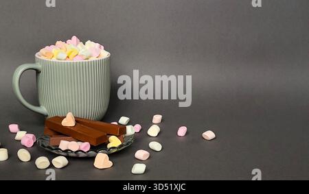 Una tazza grigia con marshmallow e cioccolato su sfondo grigio. Spazio per il testo. Foto Stock