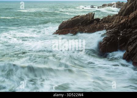 Onde oceaniche che si infrangono contro una costa rocciosa, mostrando la potenza e il movimento dell'acqua con un effetto di lunga esposizione Foto Stock