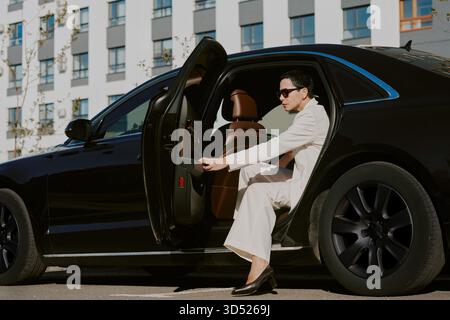 Donna di mezza età che esce dall'auto di lusso in ambiente urbano Foto Stock