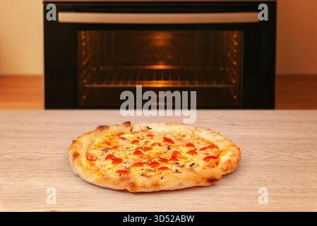 Pizza appena sfornata con salsa di pomodoro e formaggio fuso, collocata di fronte a un moderno forno da cucina, calda atmosfera casalinga Foto Stock