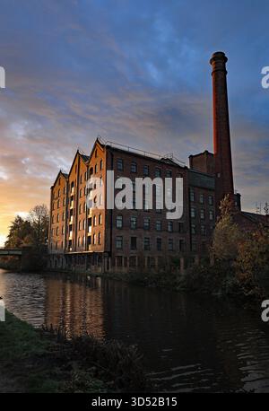 Appena dopo l'alba di una domenica di novembre il sole cattura la faccia laterale del canale e il camino del mulino di Ainscough lungo il canale di Burscough Foto Stock