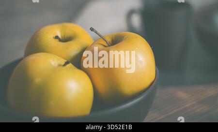 Mele rosse e verdi mature in un piatto di terracotta su un tavolo da cucina in legno. Una natura morta semplice e rustica per la fotografia di cibo Foto Stock