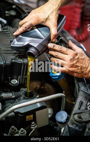 Le mani del meccanico versano olio motore nuovo nel motore di un'auto per la manutenzione Foto Stock