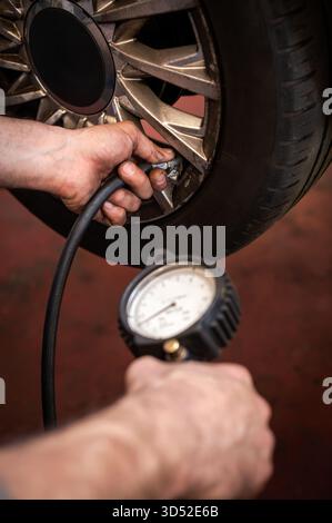 Meccanico che controlla la pressione degli pneumatici della vettura con un manometro durante gli interventi di manutenzione ordinaria Foto Stock
