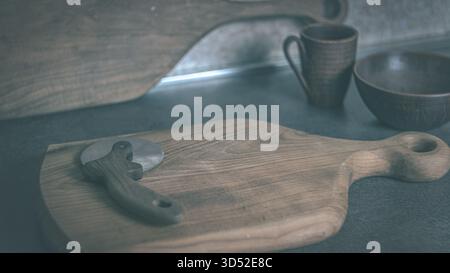 Tagliapiastrelle con manico in legno adagiato su un tagliere in legno in una cucina casalinga, semplice scena di preparazione degli alimenti rustici Foto Stock
