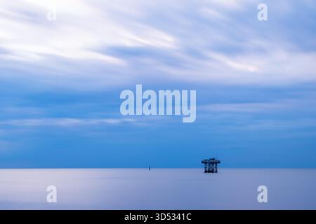 Vista a lunga esposizione di una piattaforma di raffreddamento offshore abbandonata dalla centrale nucleare di Sizewell all'alba con toni blu tenui sul mare e il cielo calmi Foto Stock