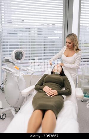 Donna di mezza età rilassata che ottiene una procedura di sollevamento ecografico professionale sulla fronte da parte di un cosmetologo in clinica. Concetto di bellezza Foto Stock