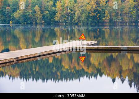 Un molo di legno si estende in un lago fermo in Svezia. Un cartello di divieto di immersione è chiaramente visibile, che indica le norme di sicurezza in questo sito di bagni pubblici. foli autunnali Foto Stock