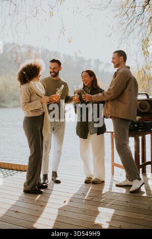 Quattro amici si riuniscono su un ponte di legno al tramonto, condividendo risate e bevande mentre si godono la bellezza della natura. Foto Stock