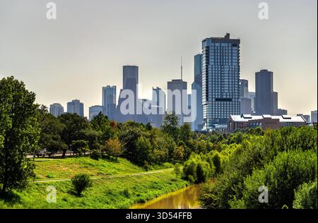Lo skyline del centro di Houston sorge sopra i lussureggianti alberi verdi e il sentiero del Buffalo Bayou Park. Il bayou marrone fangoso scorre in primo piano Foto Stock