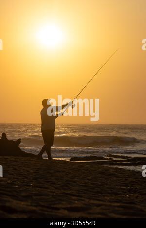 Silhouette di Person Surf Fishing al Sunset on Beach Foto Stock