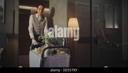 Personale alberghiero professionale che offre servizio in camera in sistemazioni di lusso. Beautiful Woman in Snow White Gloves offre colazione all'americana in camera. Servizio clienti attento, esperienza di viaggio Premium. Foto Stock