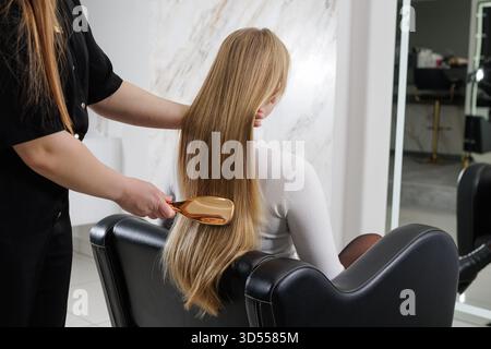 Procedura di cura dei capelli con una spazzola a paletta sui lunghi capelli biondi dritti in un moderno concetto di trattamento sano e brillante. Foto Stock