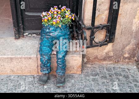 Fioriera stravagante a forma di pantaloni blu che tengono fiori colorati all'esterno dell'ingresso di un edificio. Foto Stock