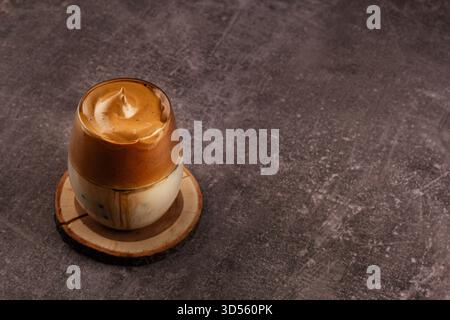 Delizioso caffè montato in una tazza di vetro trasparente, con strati cremosi su un sottobicchiere di legno. La superficie scura aggiunge un tocco caldo e invitante al caffè Foto Stock