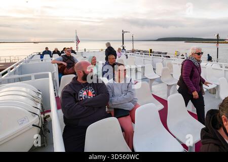 Catturata durante le tranquille ore dell'alba, questa scena mostra i passeggeri a bordo di un traghetto in partenza dall'isola di Mackinac. La nave scivola attraverso il TH Foto Stock