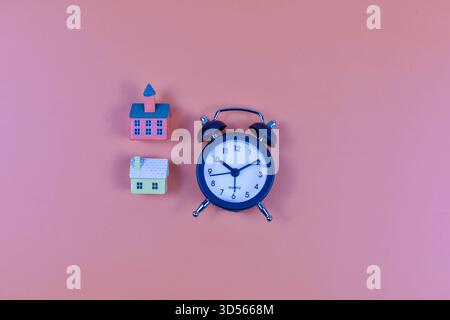 Le case modello e la sveglia su sfondo rosa rappresentano le routine quotidiane, la gestione del tempo e l'equilibrio tra la vita domestica e quella istituzionale. Foto Stock