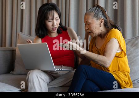 Donne asiatiche che discutono di qualcosa su un laptop mentre si siedono sul divano a casa Foto Stock