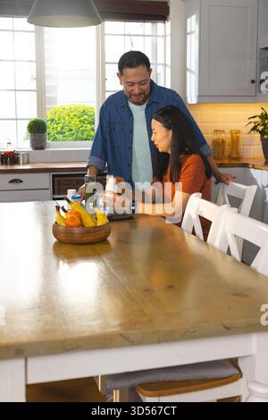 Una coppia asiatica matura si diverte a fare colazione insieme a casa, sorridendo e condividendo le conversazioni Foto Stock