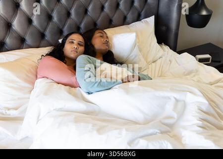Diverse donne che dormono sotto il piumone nella camera da letto con lampada, sveglia e smartphone Foto Stock